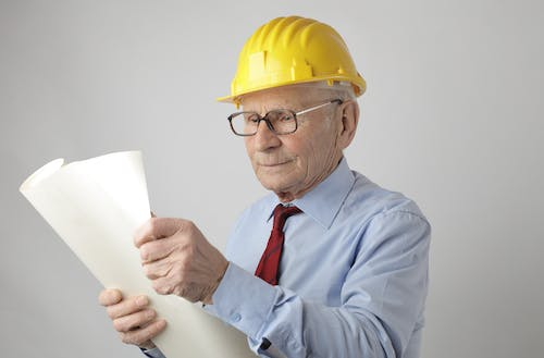a senior individual wearing a yellow hard hat while holding a sheet of paper